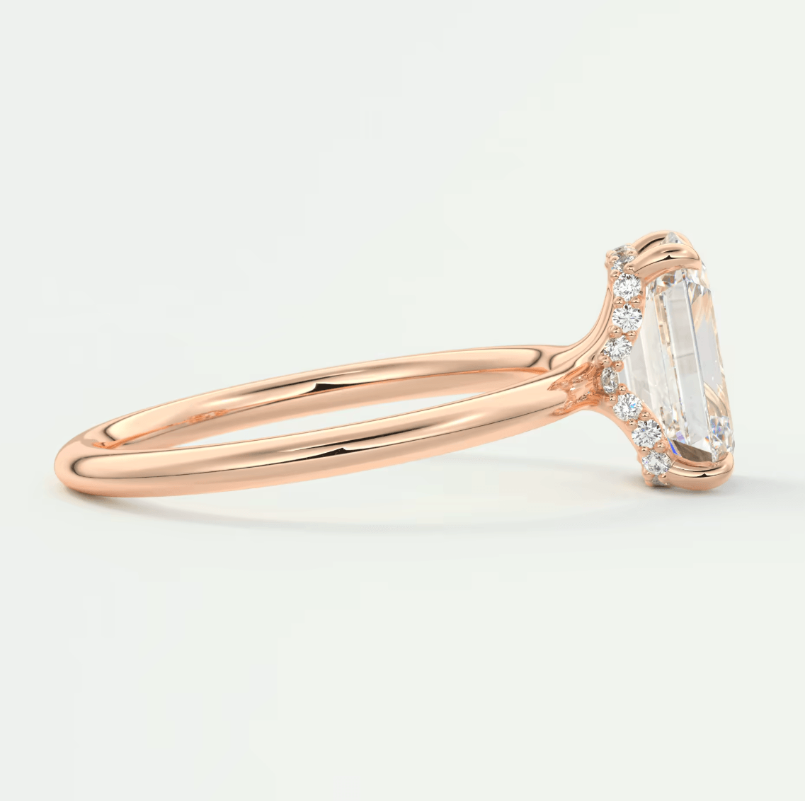 18k rose gold engagement ring with an emerald-cut diamond and small round diamonds on the band.