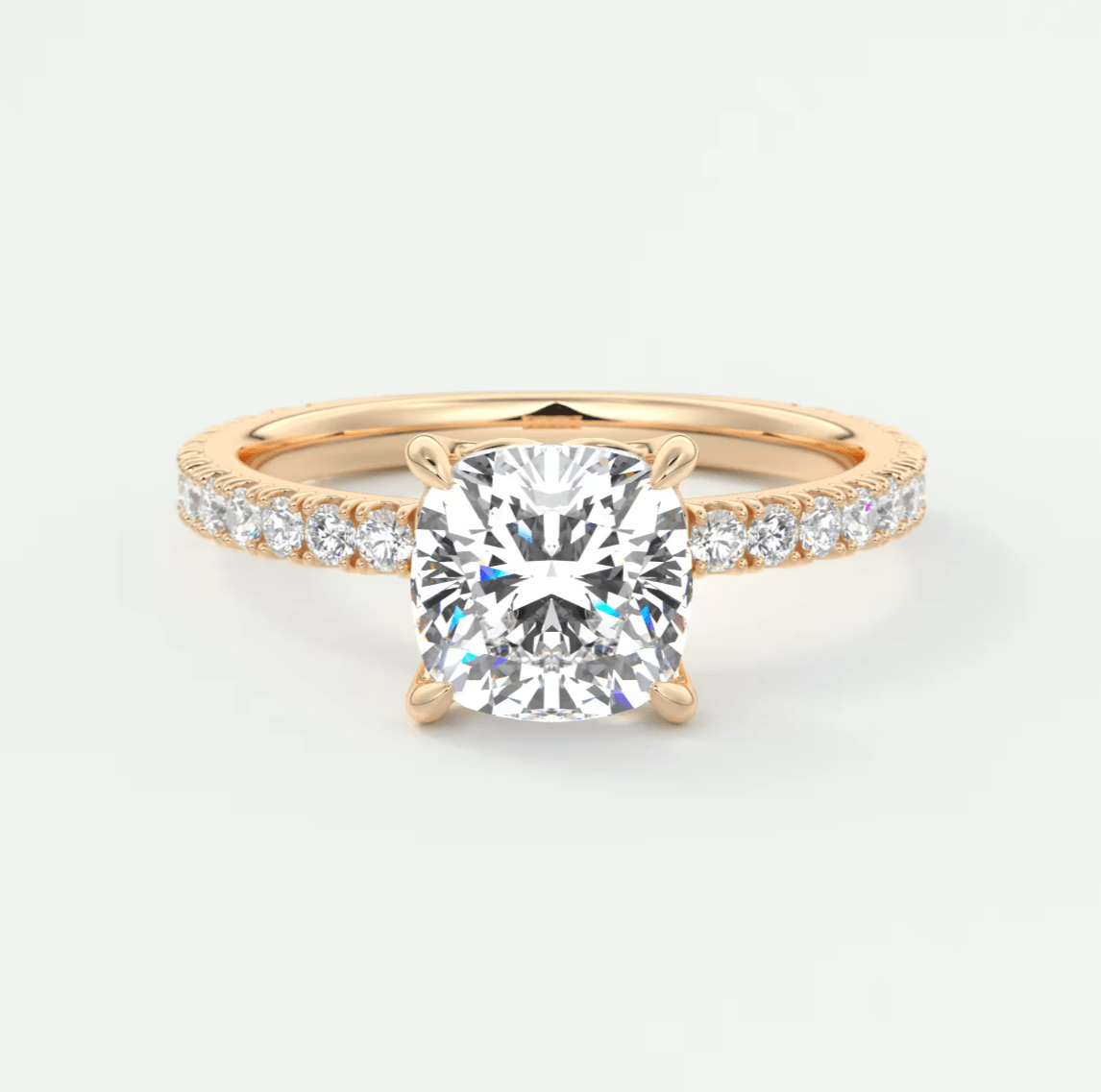 18k rose gold diamond engagement ring with a cushion-cut center stone and pavé set diamonds on the band.