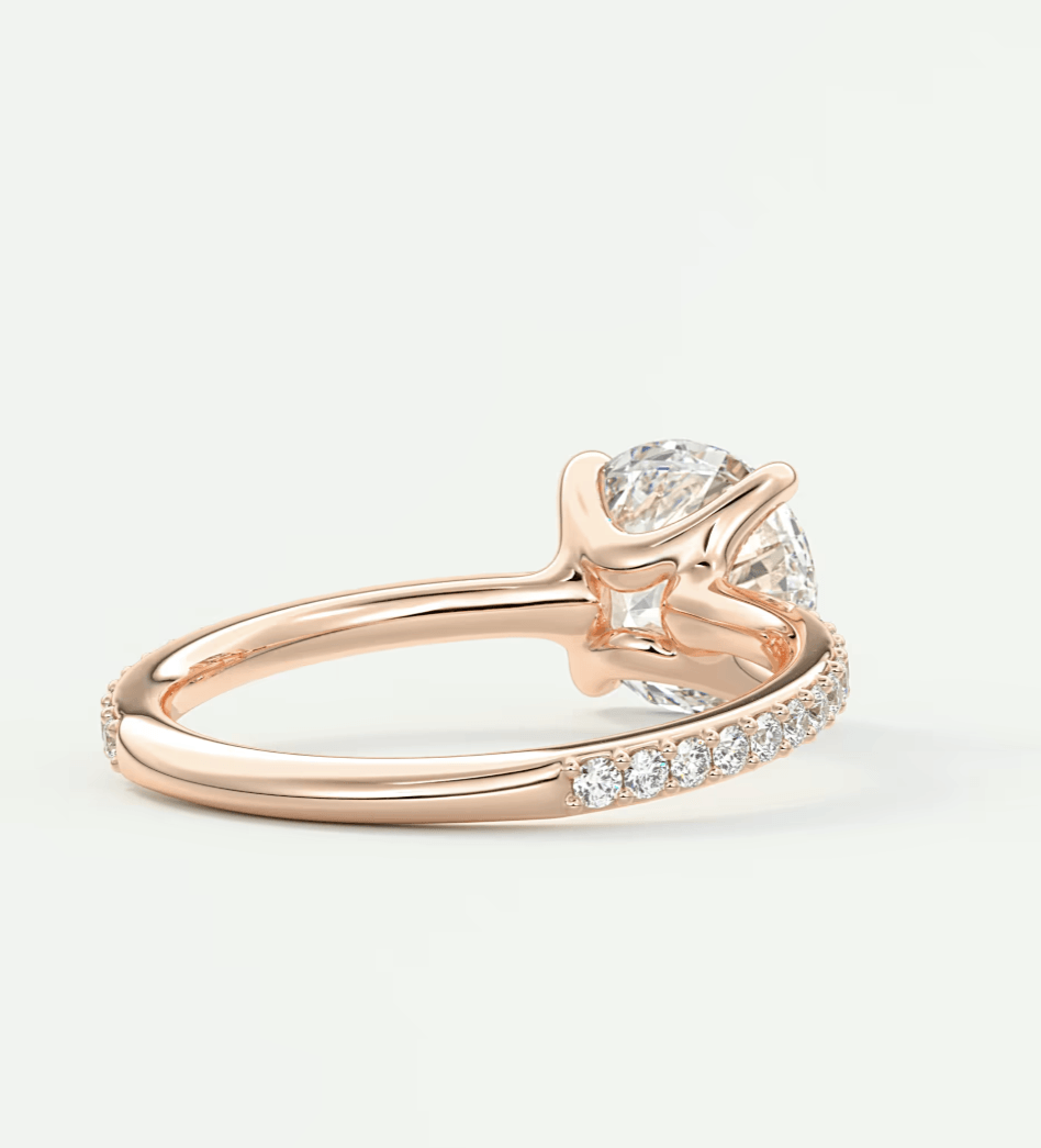 18-karat rose gold diamond engagement ring with a solitaire design and pave-set diamonds on the band.