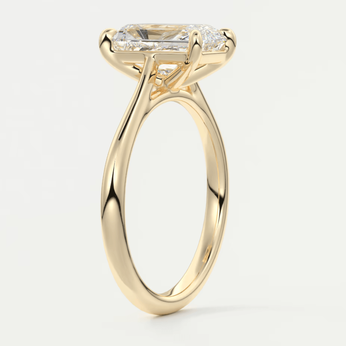 18k yellow gold emerald-cut diamond engagement ring with a delicate, swirling band.