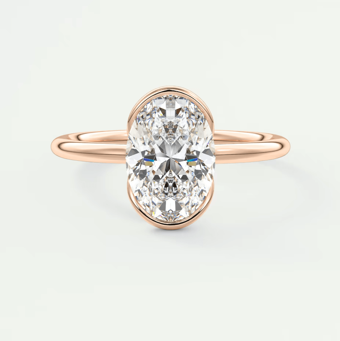 Rose gold oval diamond engagement ring with a bezel setting.