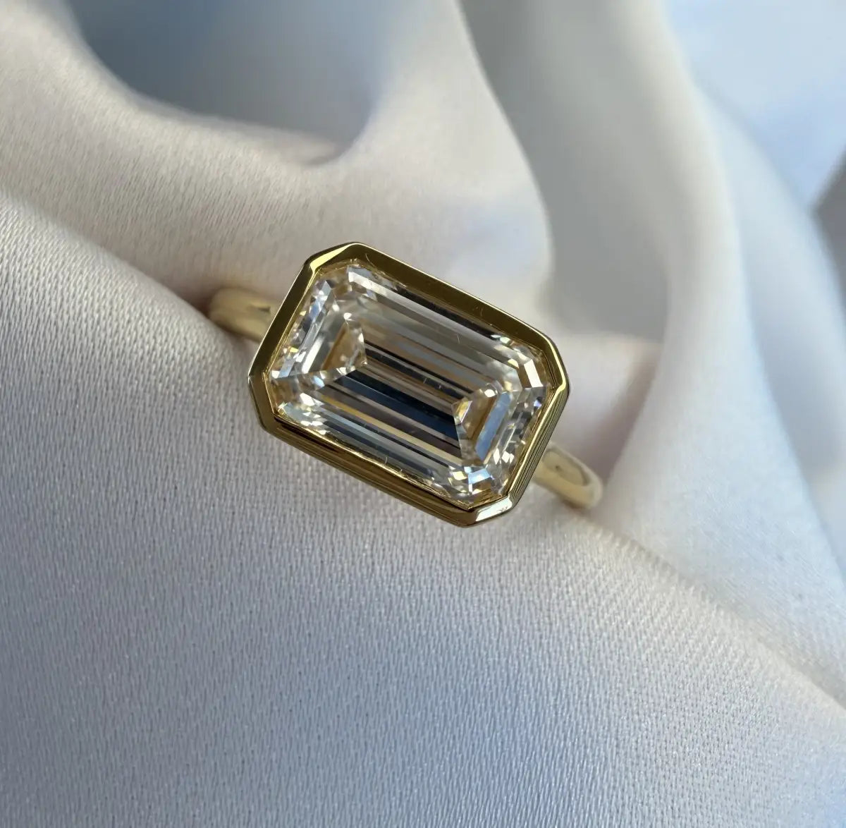 Gold ring with a large emerald-cut diamond on a white fabric background