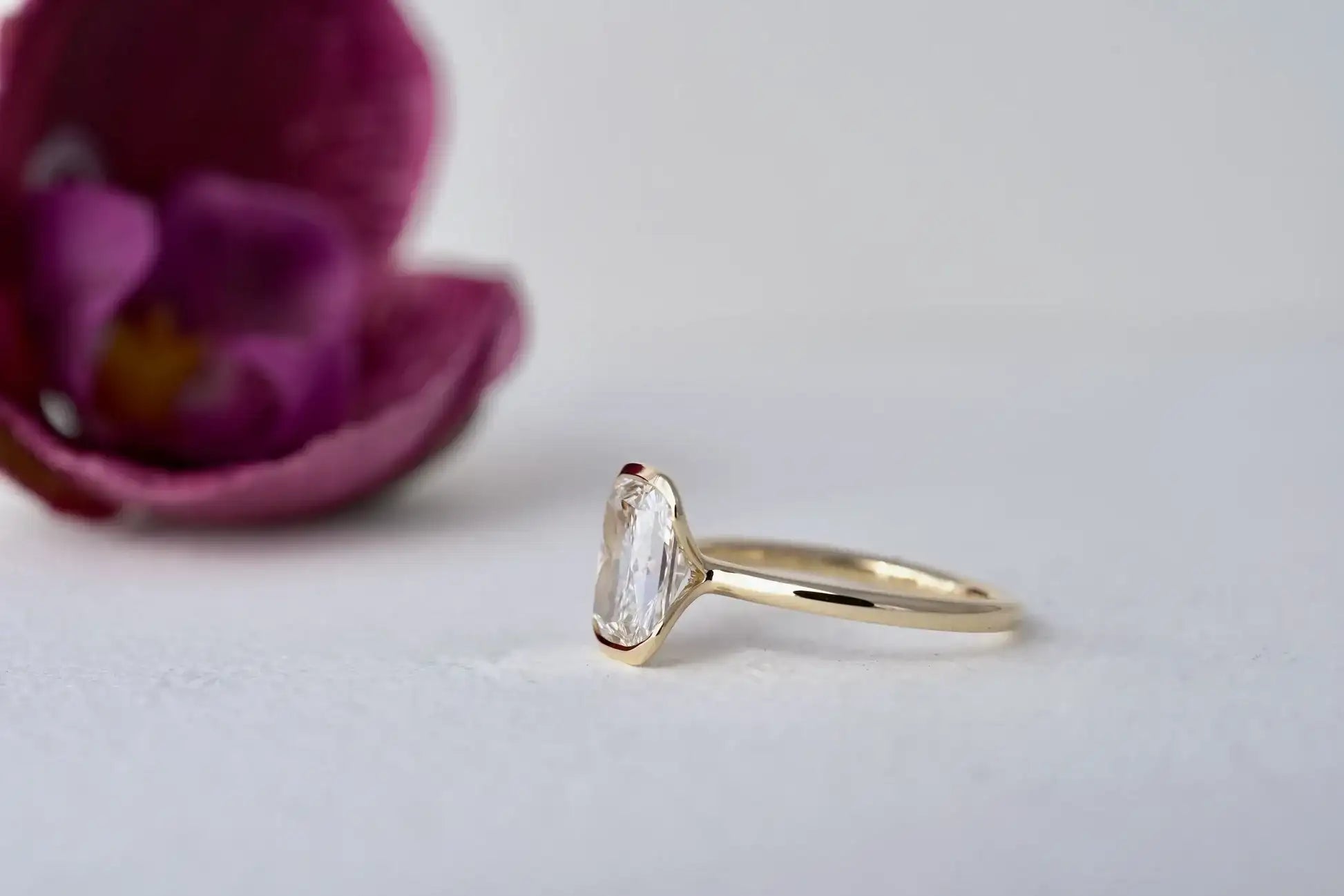 Gold ring with a diamond next to a purple flower on a light background