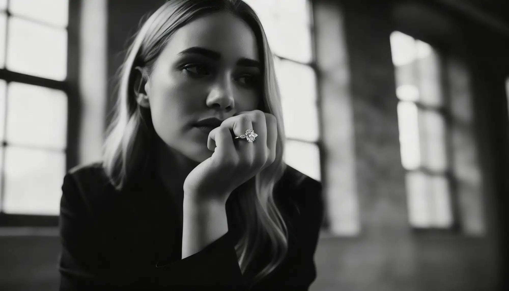 Black and white portrait of a woman with a ring on her finger, sitting indoors.