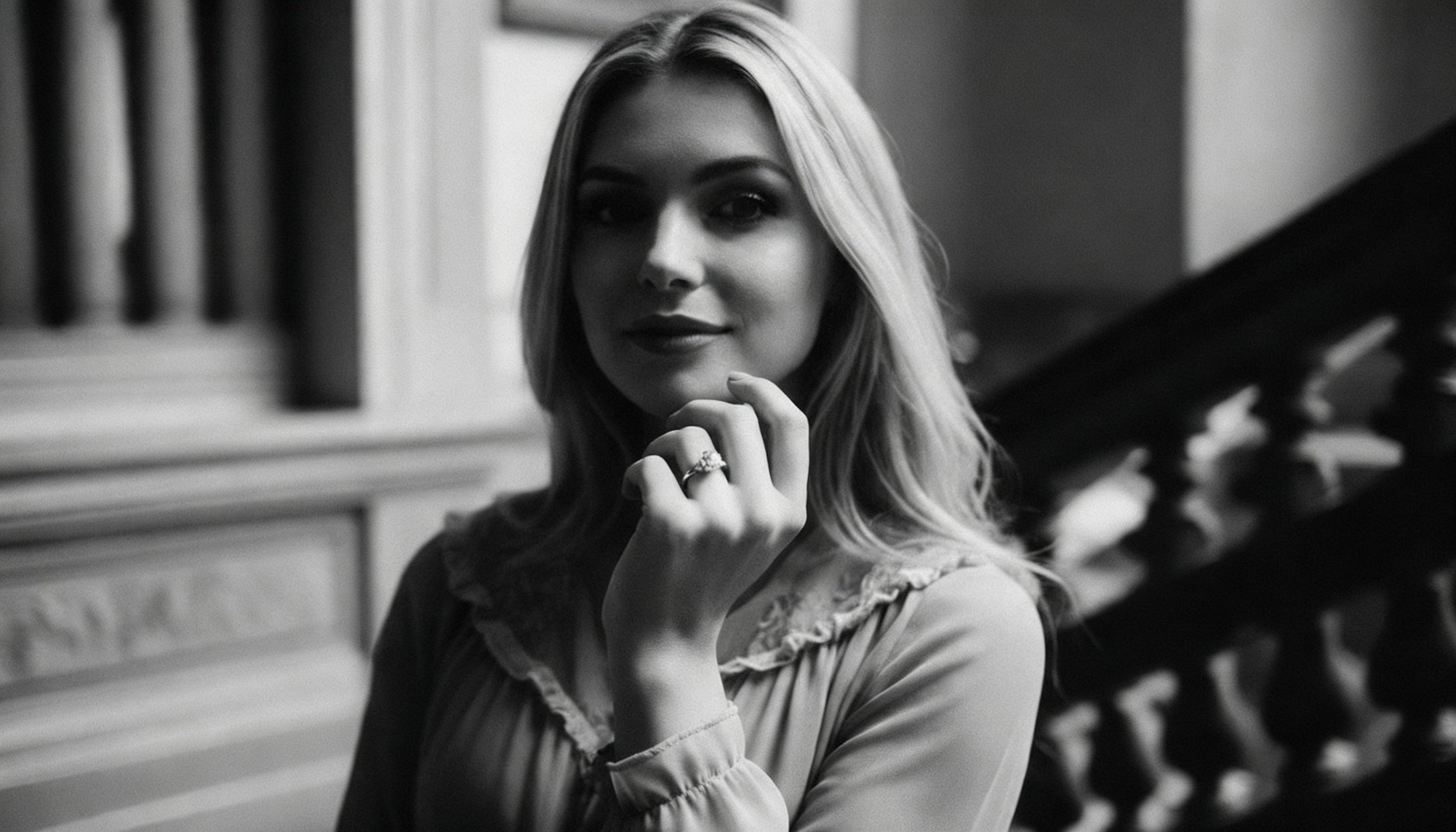 Black and white photo of a woman with her hand on her chin, standing indoors.