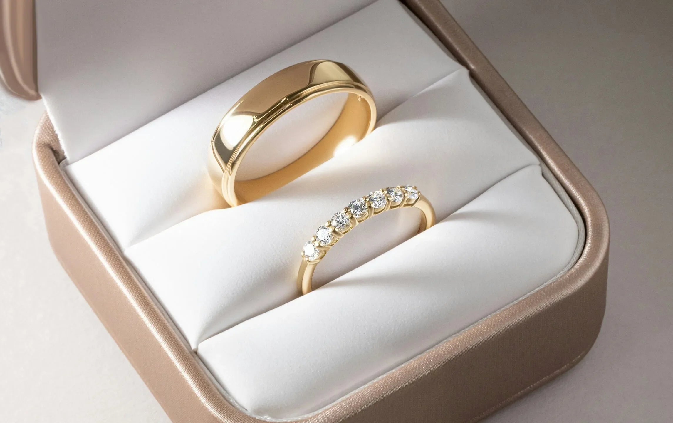 Two gold rings in a jewelry box with a white interior
