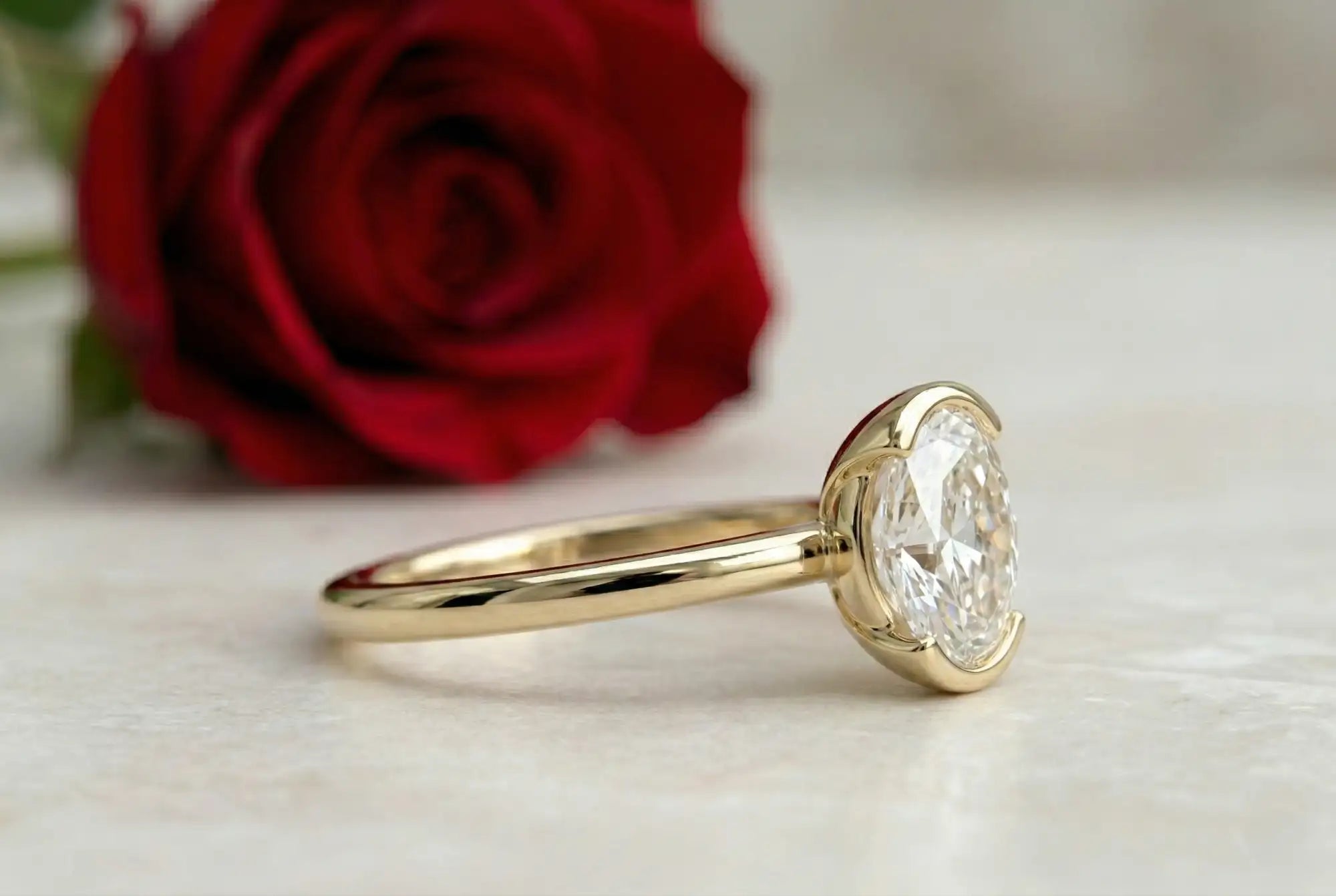 Gold ring with a diamond next to a red rose on a light background