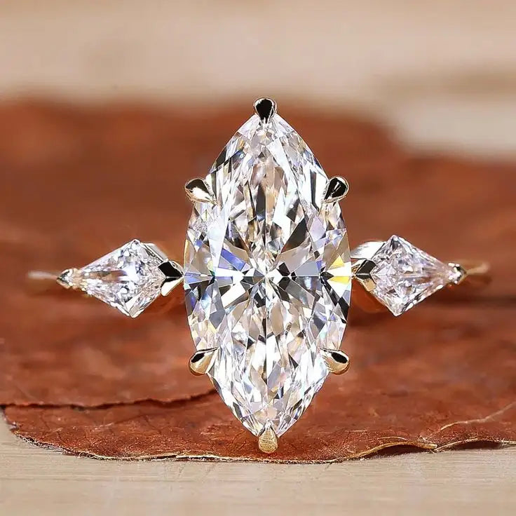 Diamond ring with marquise-shaped center stone and square stones on a brown leaf background