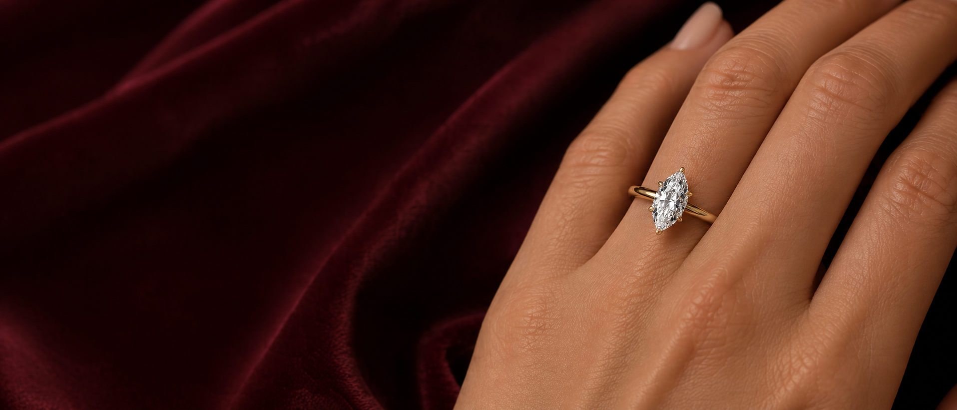 Hand wearing a diamond ring on a dark red fabric background