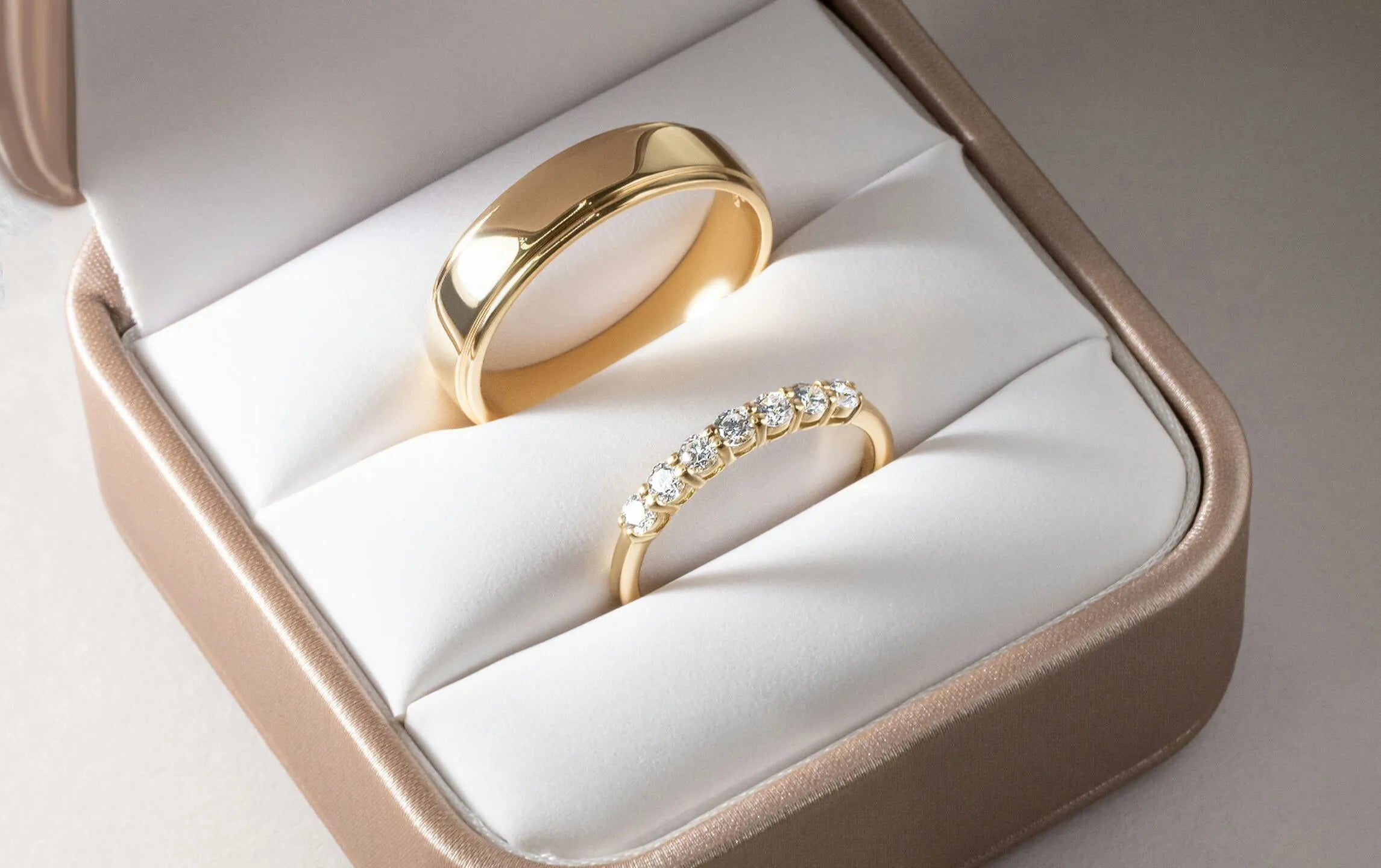 Two gold rings in a jewelry box with a white interior