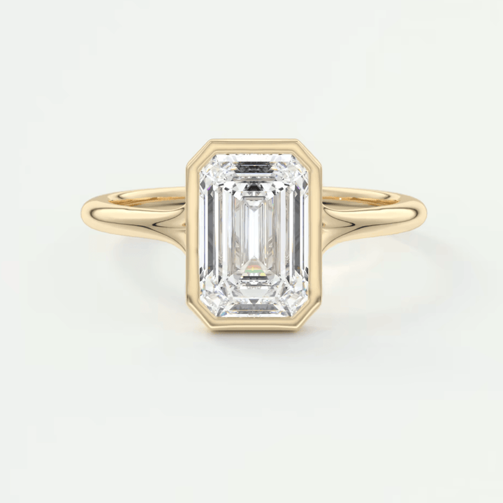 An emerald-cut diamond or moissanite ring with a thin gold band and a bezel setting, showcasing a modern, airy design.