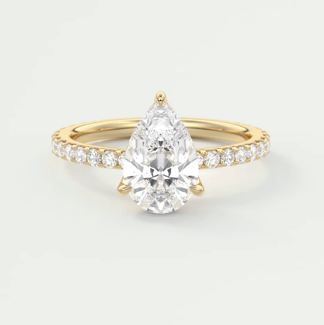 Pear-shaped diamond engagement ring with gold band and white diamonds set in a halo design.