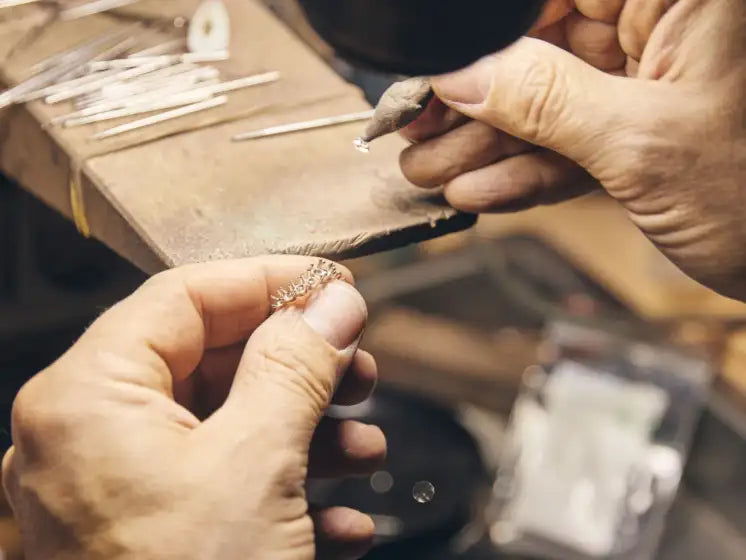Jeweler working on a piece of jewelry with tools and materials in the background