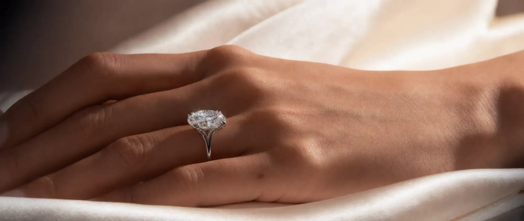 Hand wearing a diamond ring on a soft fabric background