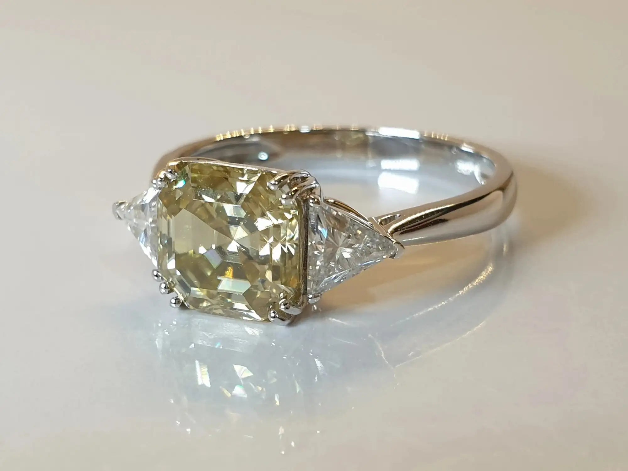 Diamond ring with a yellow diamond and triangle-shaped gemstone on a light background