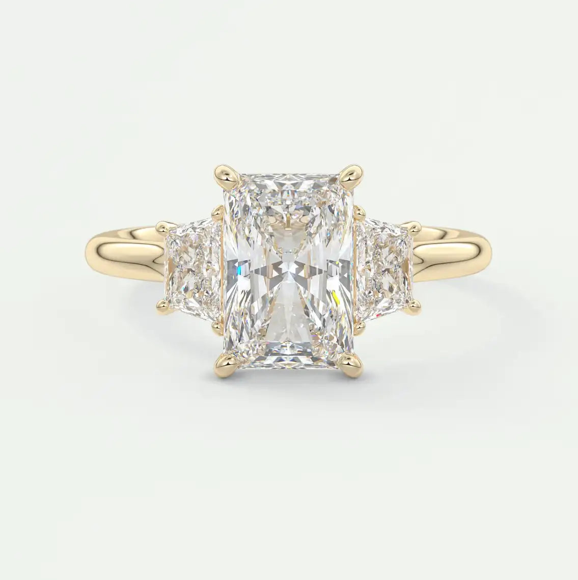 A radiant emerald-cut diamond ring set in a sleek yellow gold band, flanked by two smaller triangular diamonds on either side.