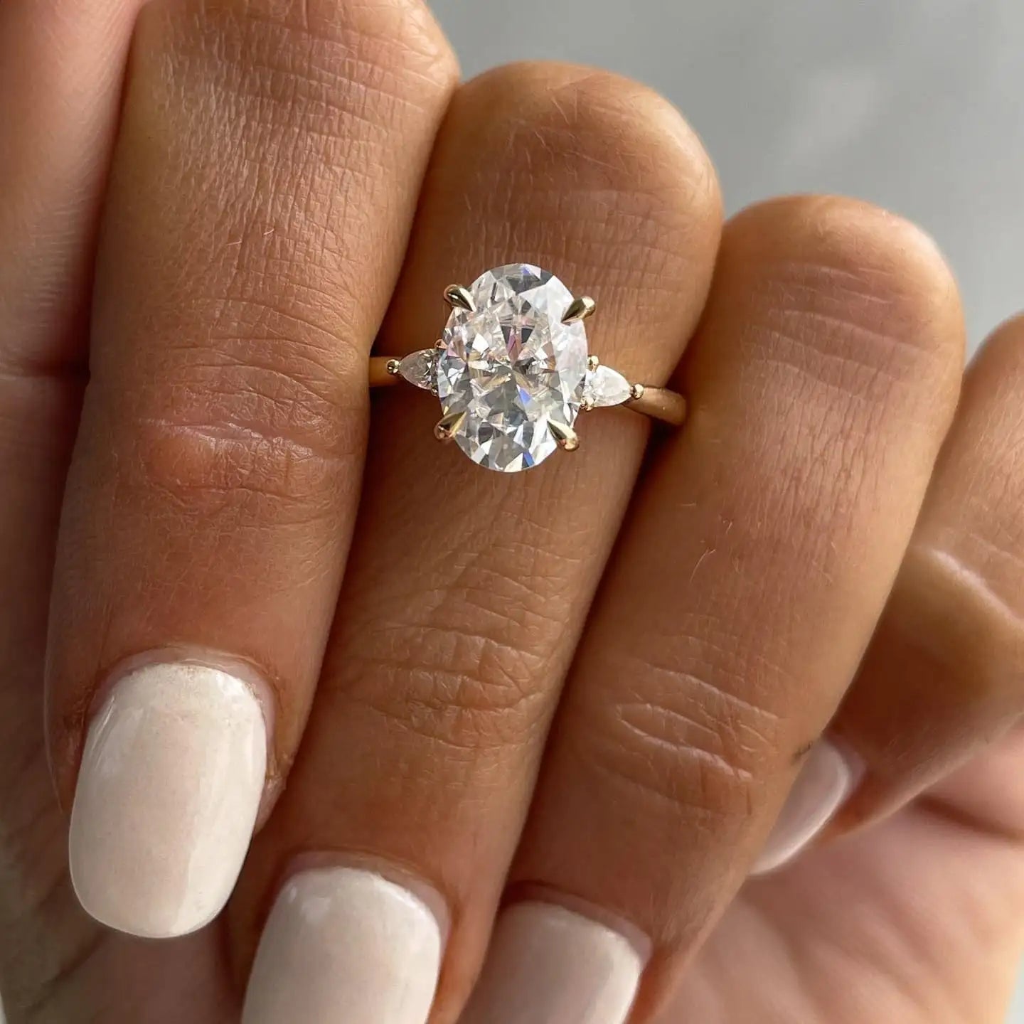 A radiant oval-cut diamond engagement ring set in a delicate gold band, accented with two smaller pear-shaped diamonds on either side.