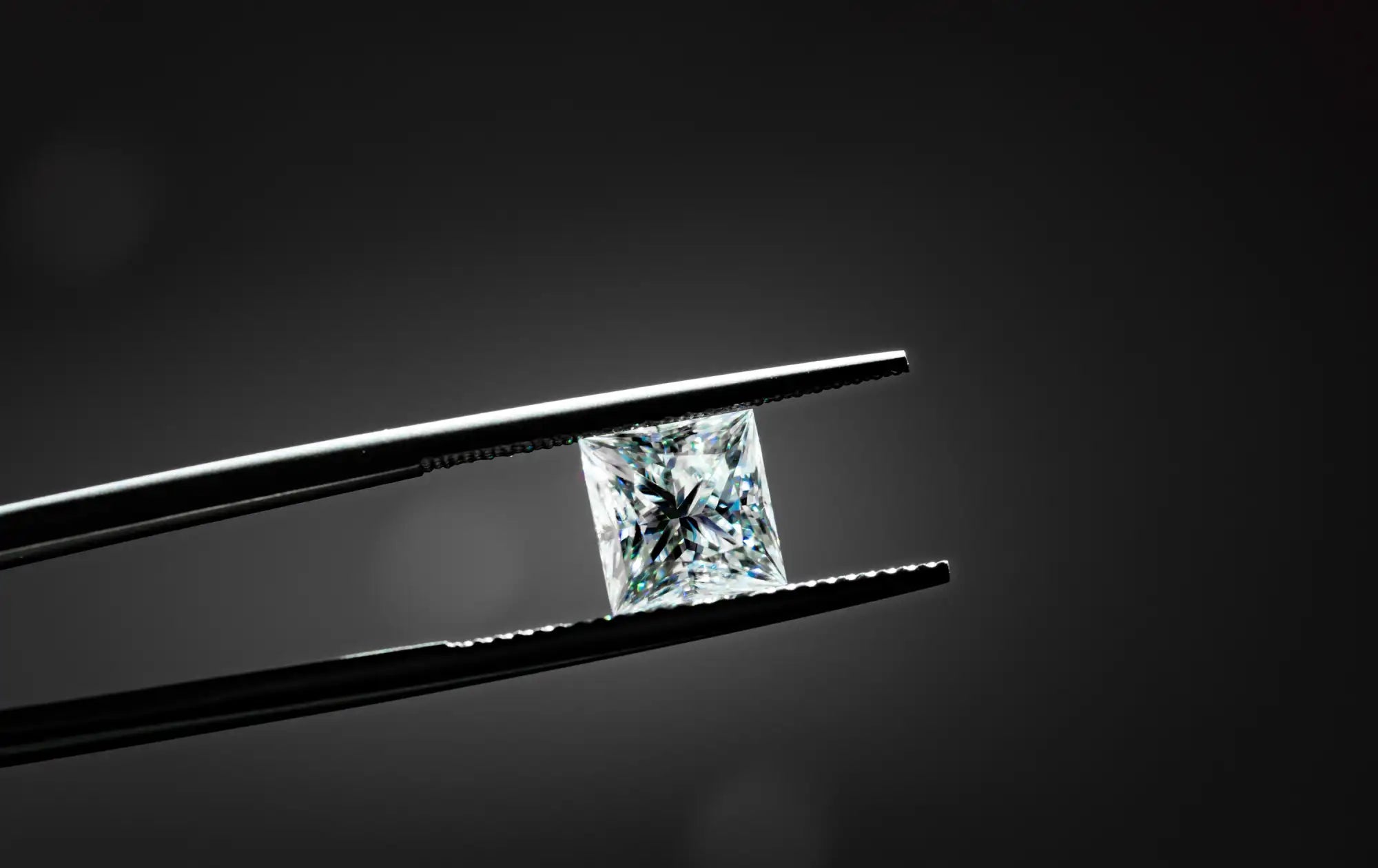 Diamond held between tweezers against a dark background