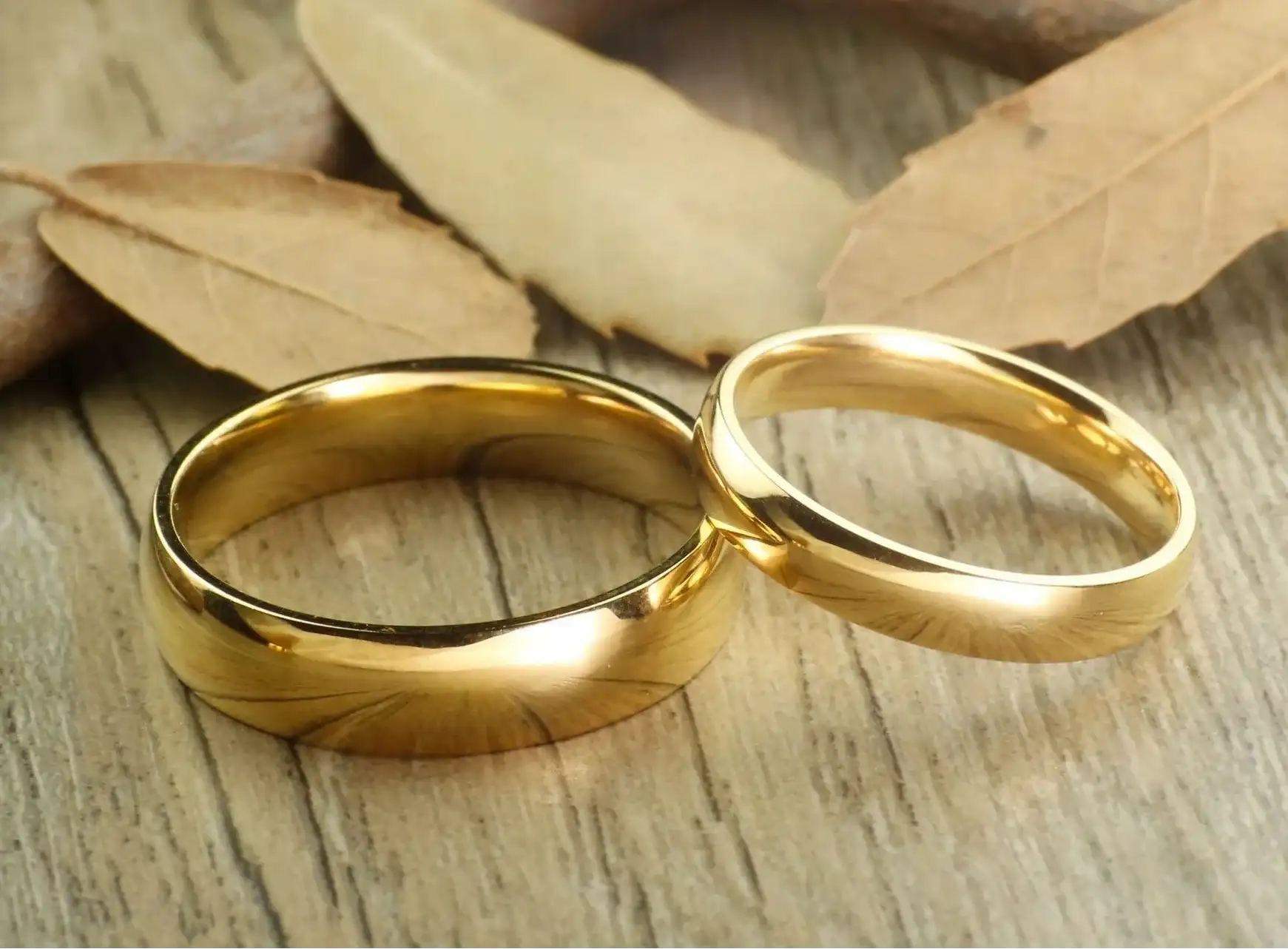 Two gold rings on a wooden surface with leaves in the background
