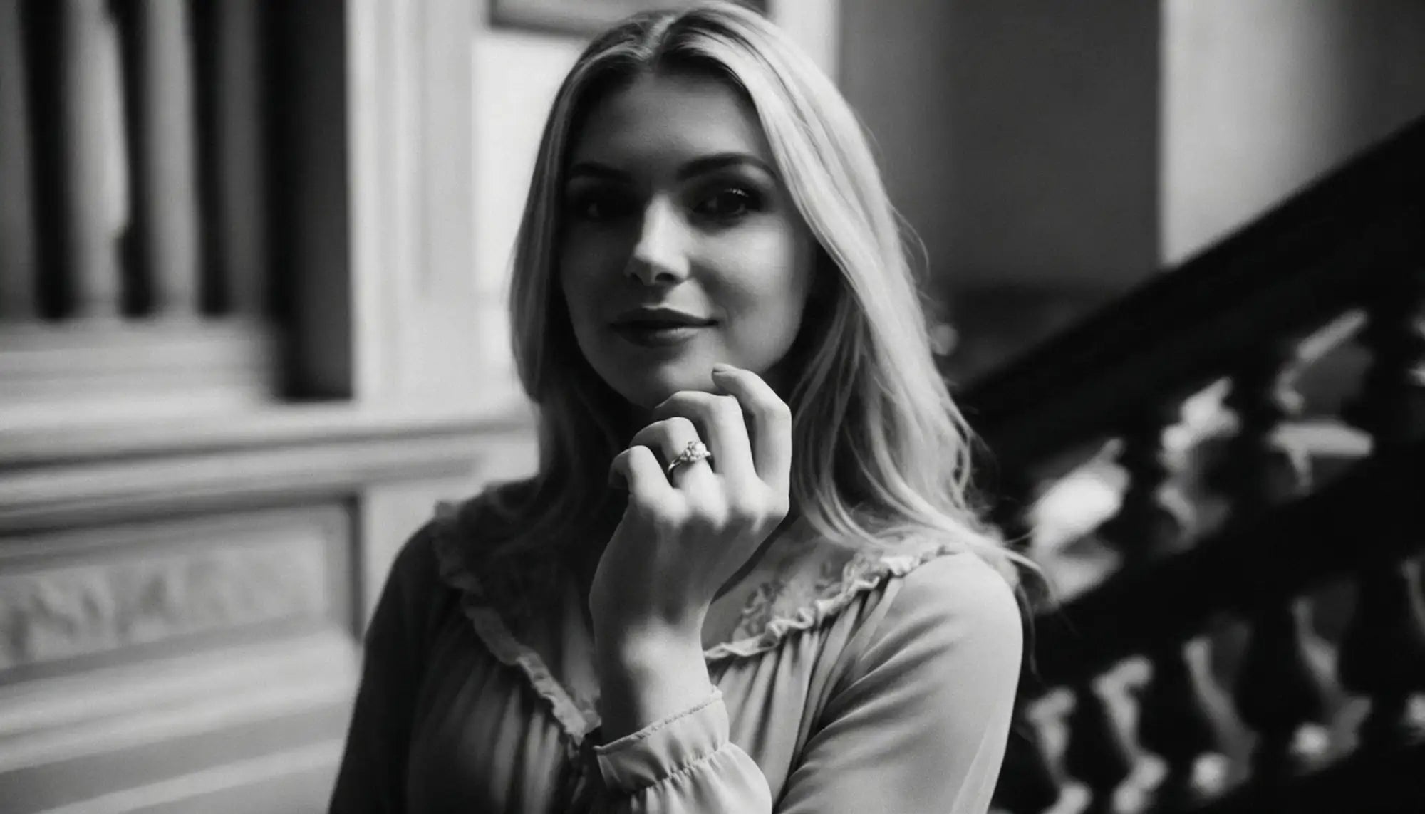 Black and white photo of a woman with her hand on her chin, standing indoors.